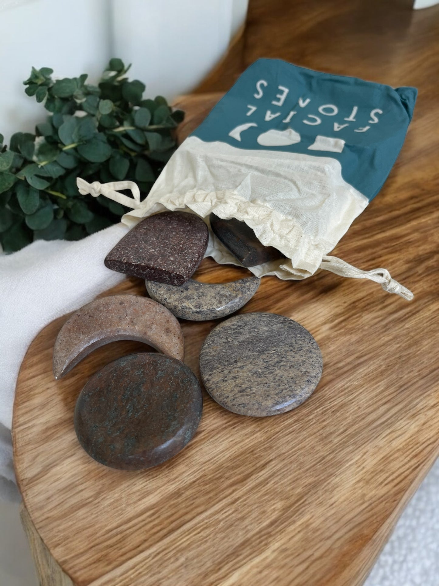 Set of stones on a wooden board with a drawstring bag labeled 'Facial Stones' in the background.
