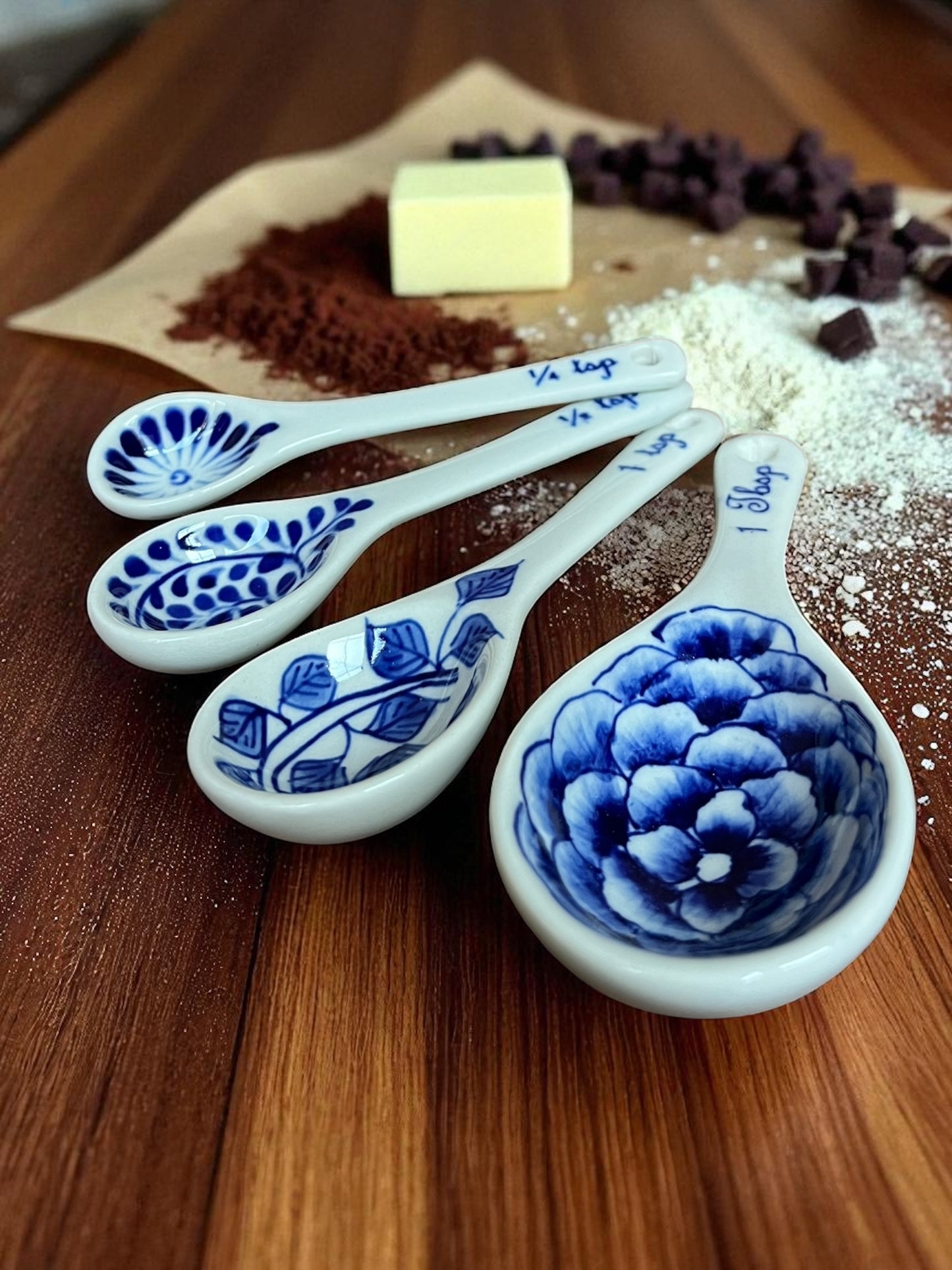 four hand-painted blue floral measuring spoons with an assortment of baking ingredients on parchment paper