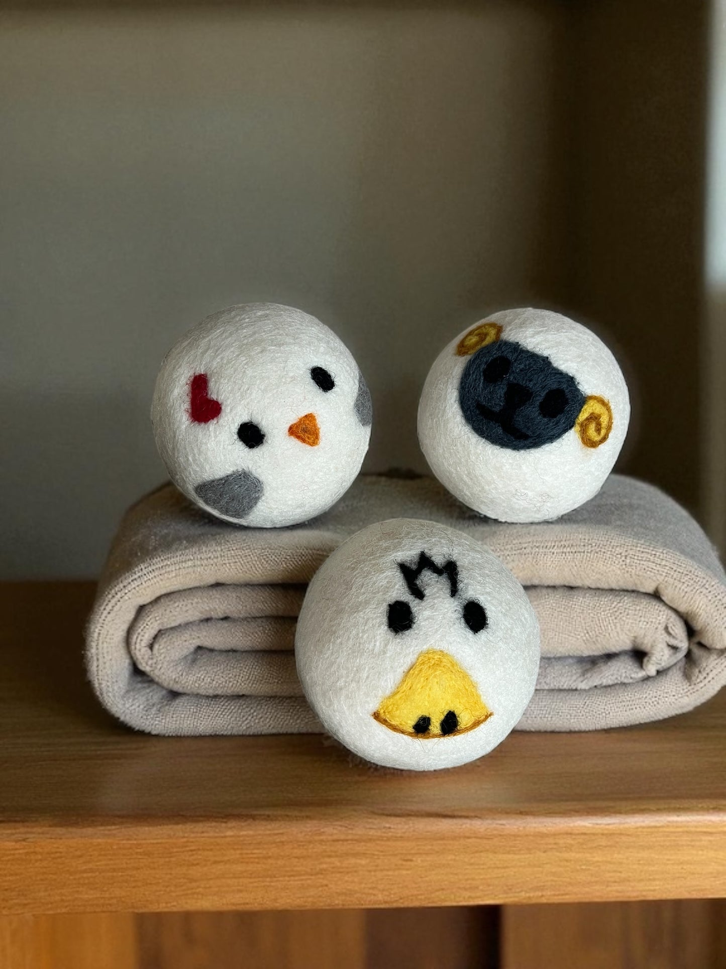 three wool laundry balls – duck, chicken, sheep on a folded towel