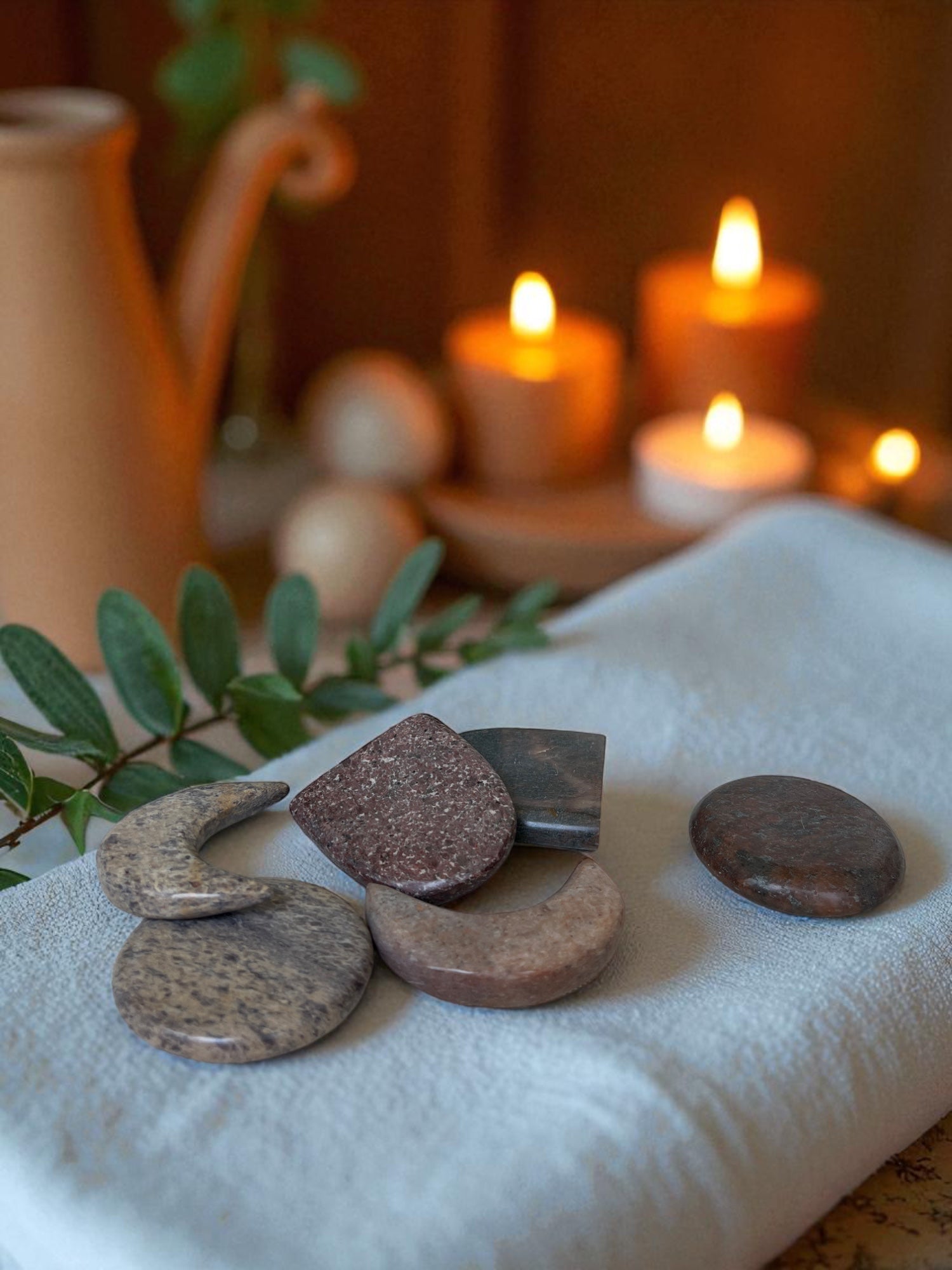 Decorative stones on a white cloth with candles and a teapot in the background
