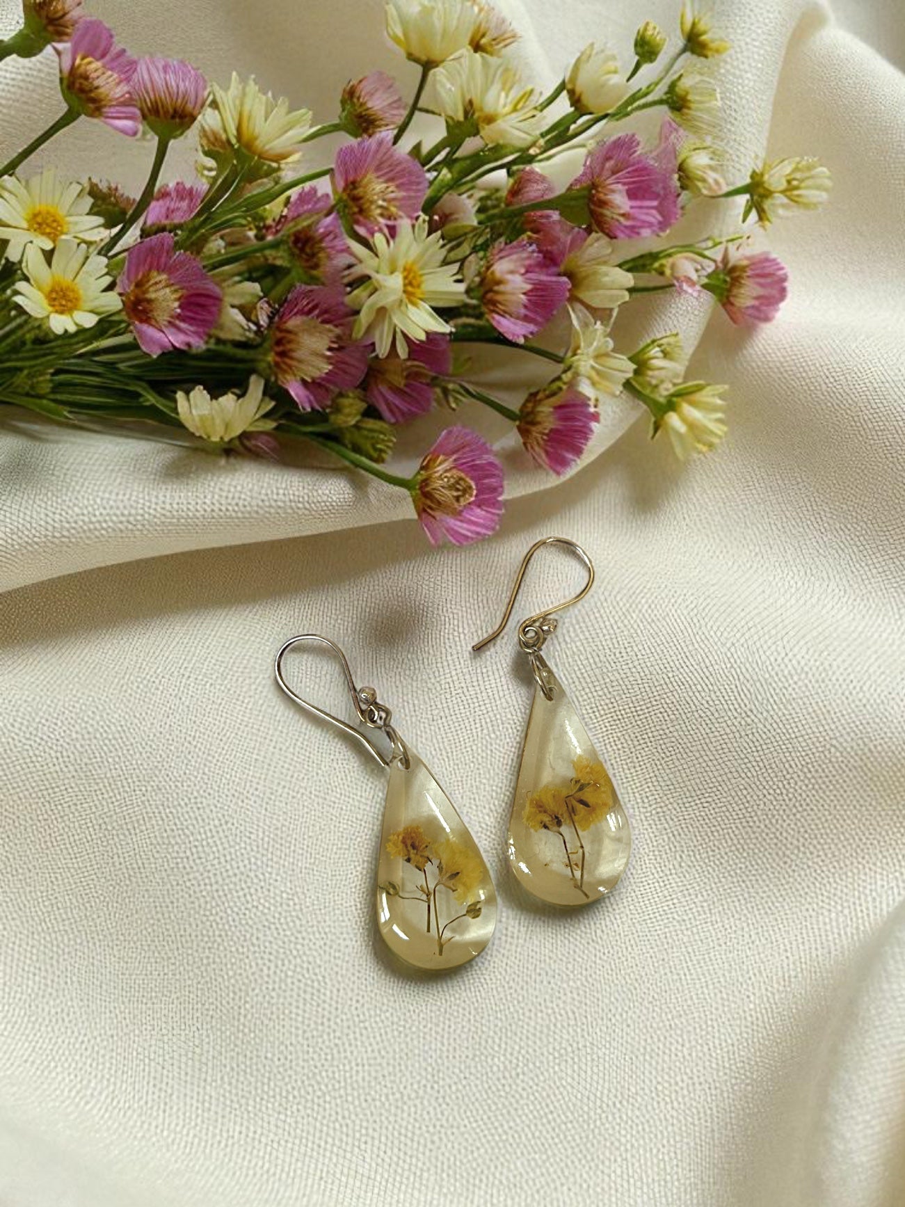 Teardrop-shaped earrings with floral design on a beige fabric background