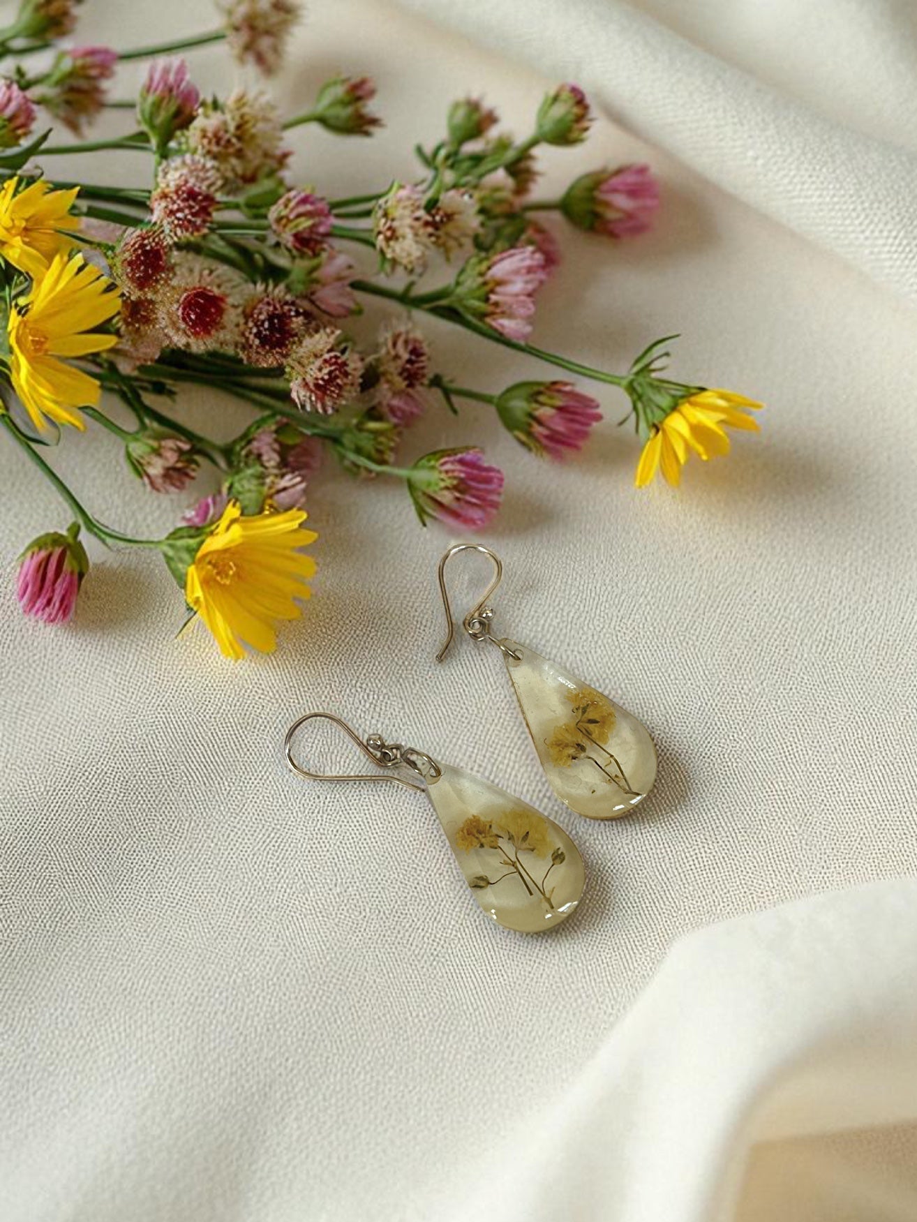 Teardrop-shaped earrings with floral design on a white fabric background with flowers.