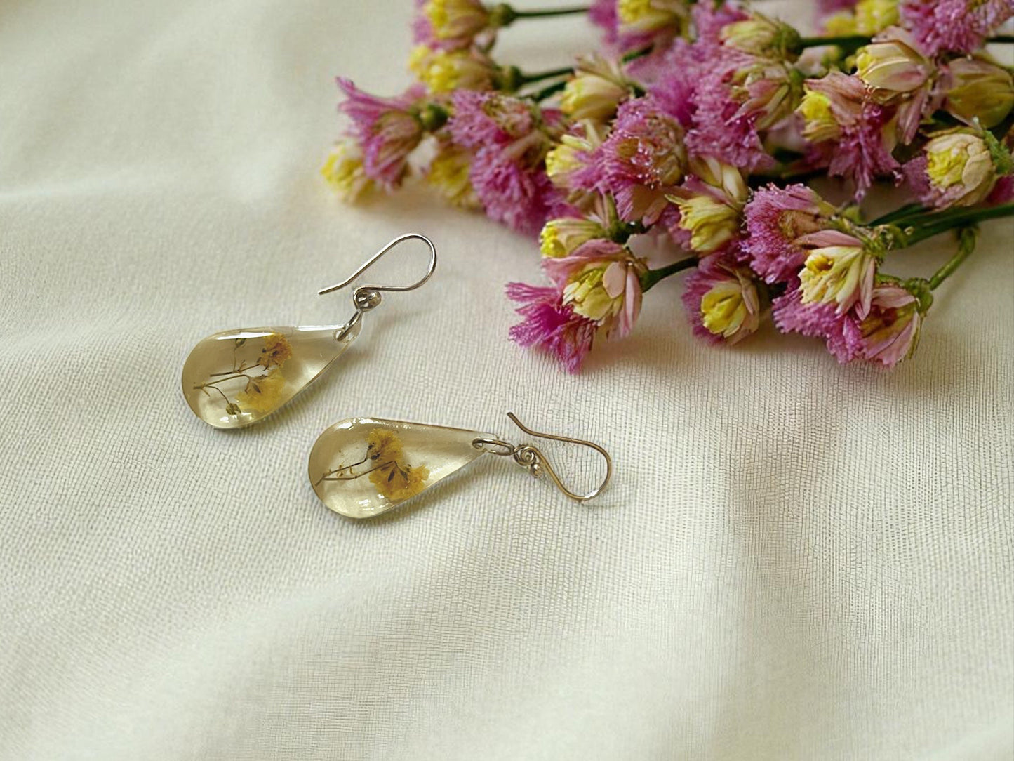 Teardrop-shaped earrings with floral elements on a light fabric background