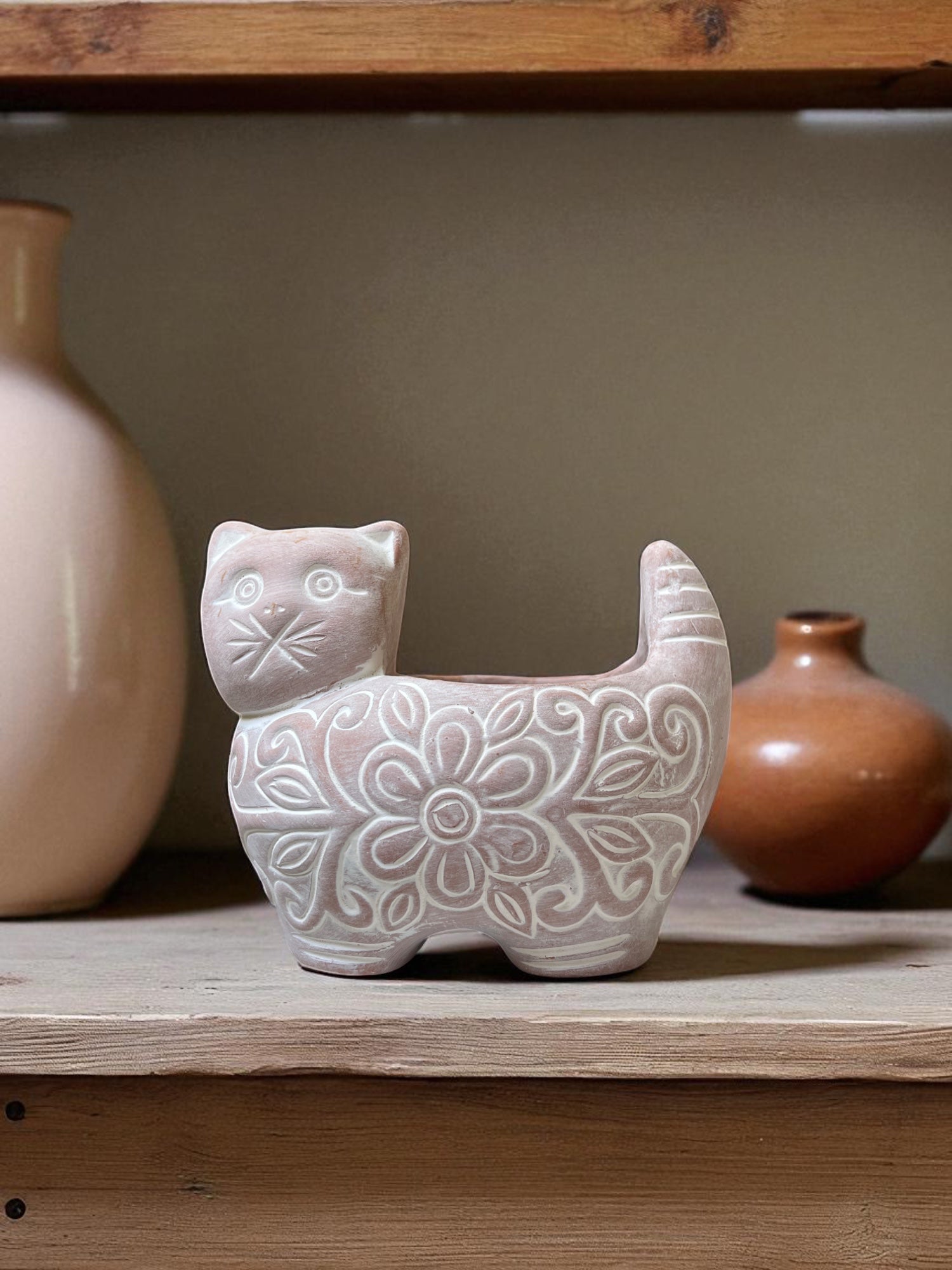Ceramic cat-shaped vase with floral patterns on a wooden shelf with other decorative items.