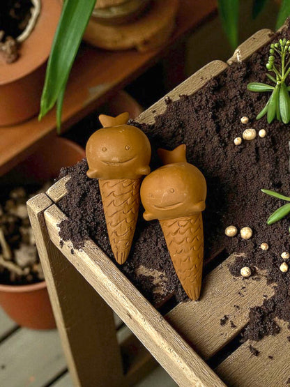 two whale-shaped watering spike rest on a garden table covered in planting soil