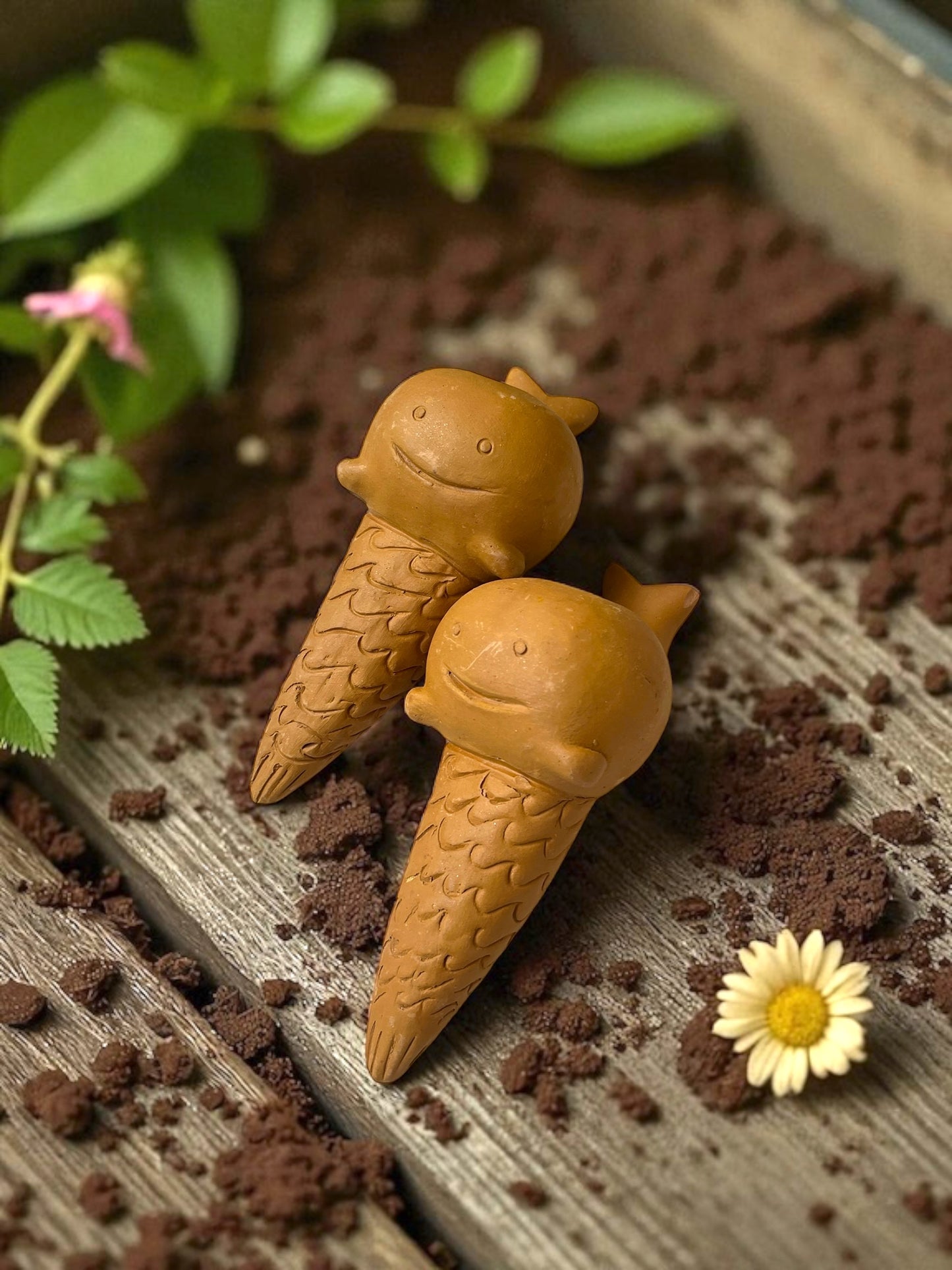 two whale-shaped watering spike rest on a garden table covered in planting soil