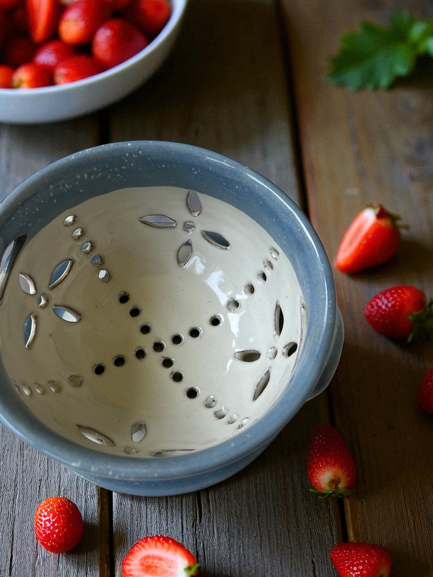 blue and white ceramic colander on a wood table with fresh strawberries