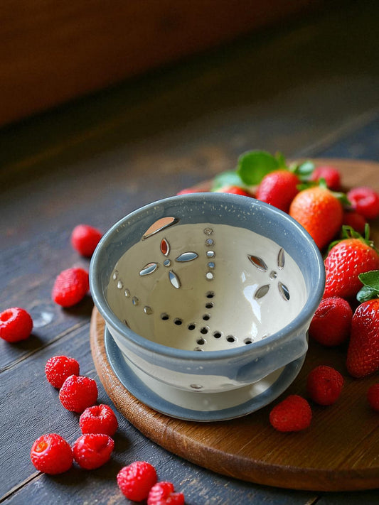 blue and white ceramic colander on a wood table with fresh strawberries and raspberries