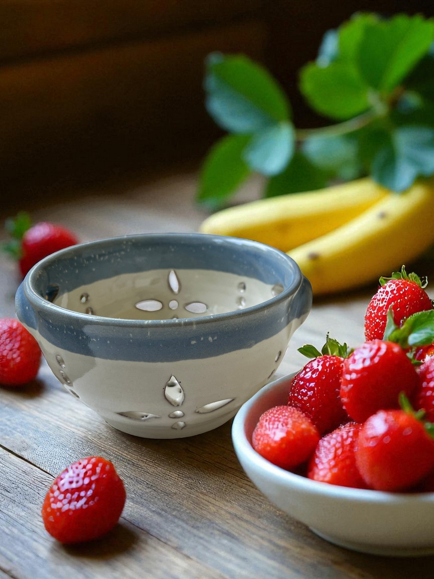 blue and white ceramic colander on a wood table with fresh strawberries and bananas