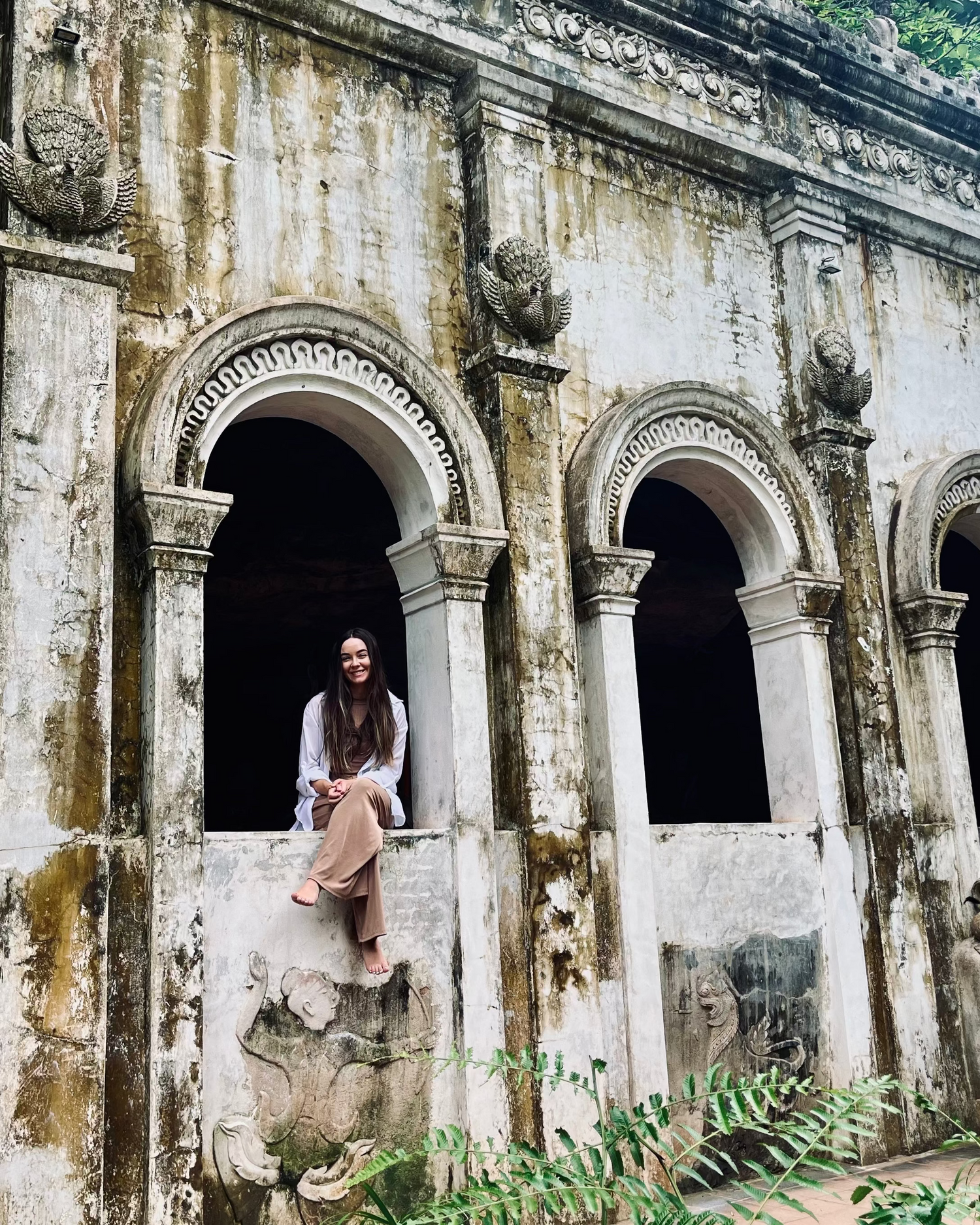 Woman sitting in an ornate stone building surrounded by greenery