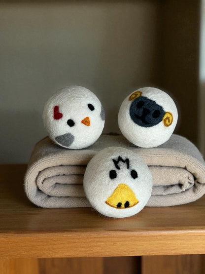three wool laundry balls – duck, chicken, sheep on a folded towel