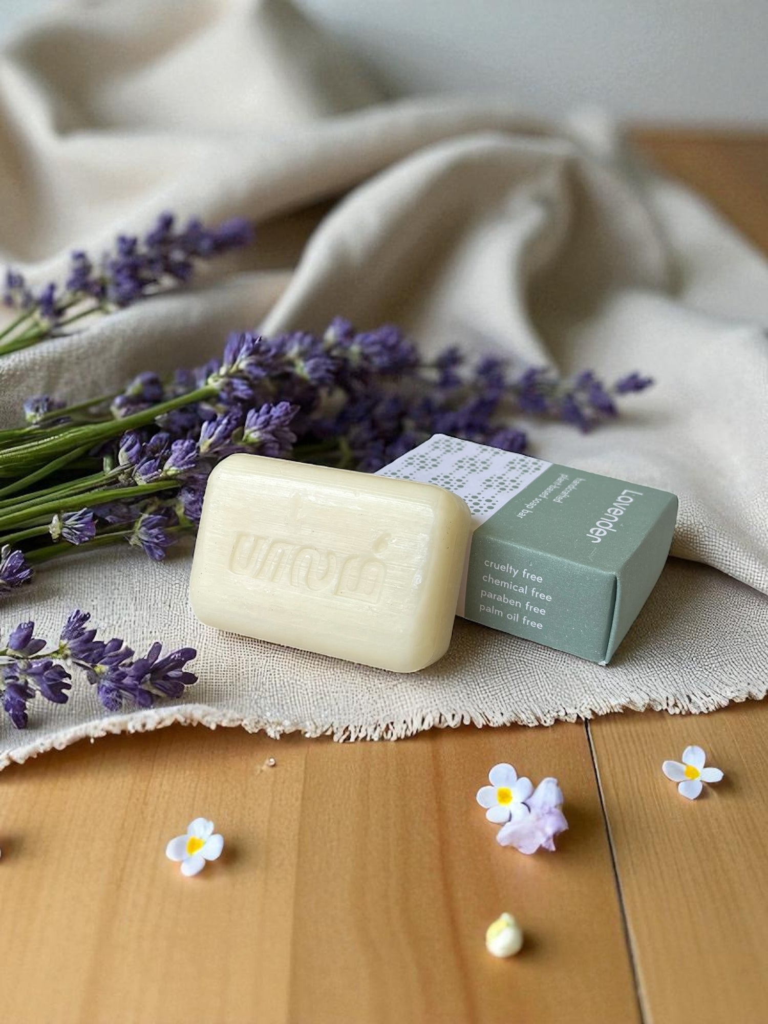 lavender soap on a light wood table with a linen cloth and purple and white flowers
