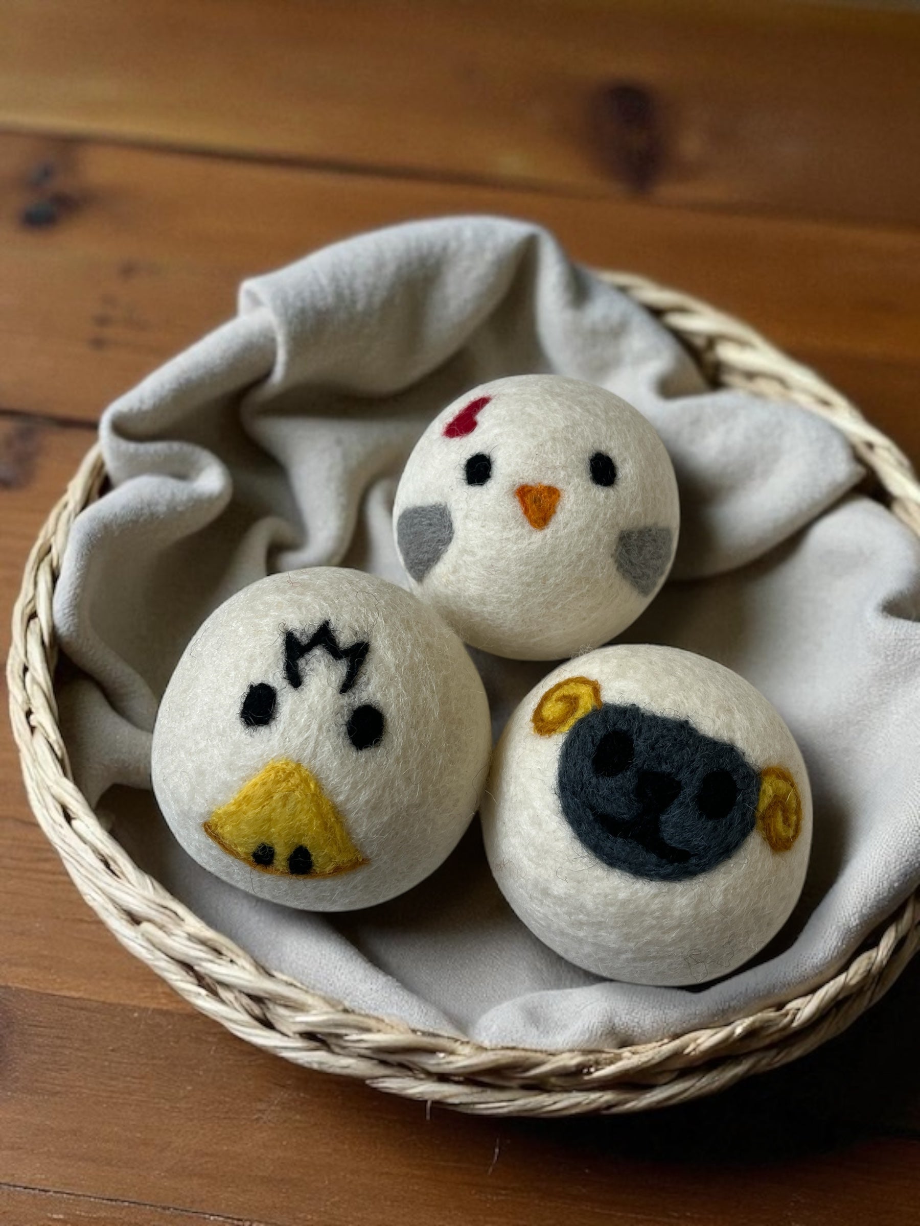 three wool laundry balls – duck, chicken, sheep – in a woven basket with a linen cloth