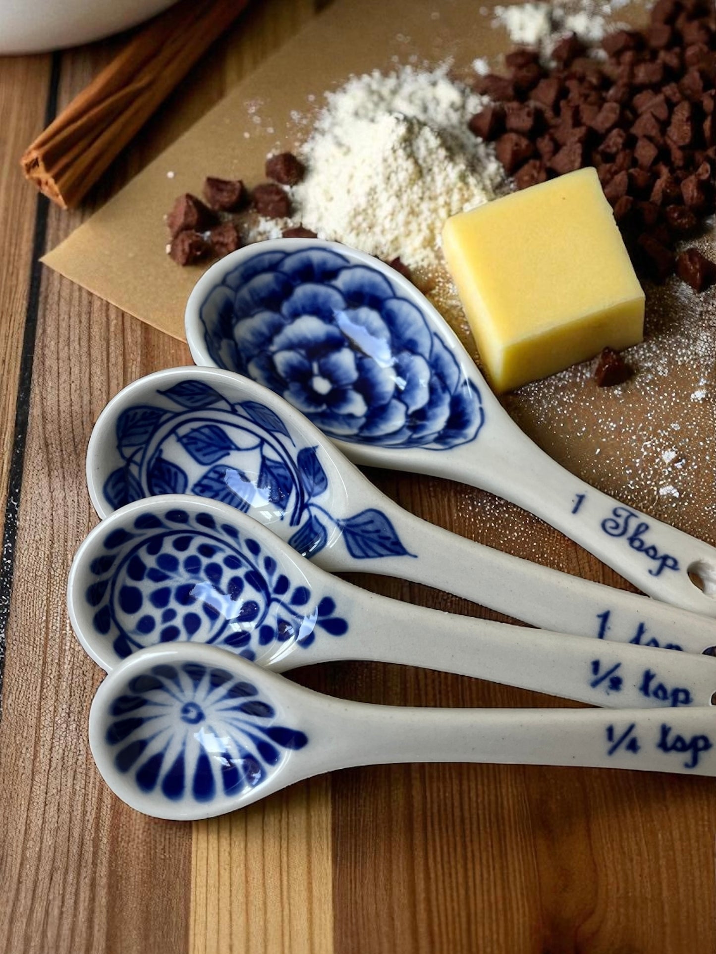 four hand-painted blue floral measuring spoons with an assortment of baking ingredients on parchment paper