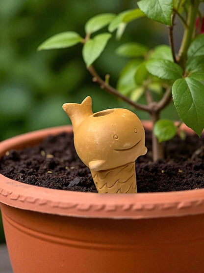 a whale-shaped watering spike pokes out of the soil of a potted plant